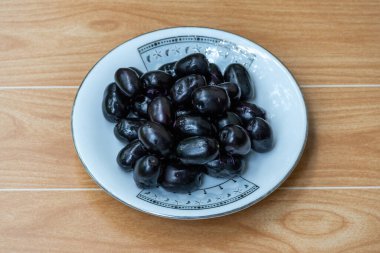 Beyaz tabakta taze siyah erikler, ahşap arka plan. Lezzetli Java eriği, Jamun meyvesi (Syzygium cumini) antioksidan açısından zengin.