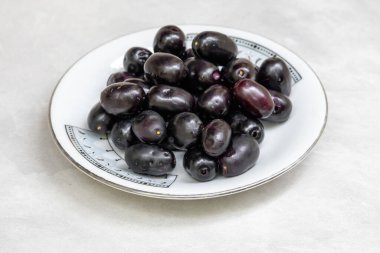 Beyaz tabakta taze siyah Java erikleri. Sağlıklı jamun meyvesi, Malabar eriği, jambul, jambolan olarak da bilinir..