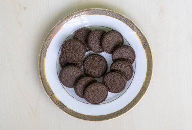 Beyaz tabakta servis edilen çikolatalı kremalı sandviç bisküvileri, ahşap arka planda. Çok lezzetli bir ikram. Üst görünüm.