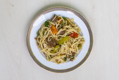 Biftek, domates, seramik tabakta yeşil biber ve yenmeye hazır lezzetli erişteler. Ahşap arkaplanda üst görünüm.