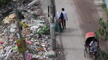 Kishoreganj, Bangladeş - 18 Haziran 2025 - Bangladeş 'te yol kenarındaki çöp yığını. Öğrenciler geçiyor, fayton geçiyor. Çevre kirliliği, kötü atık yönetimi.