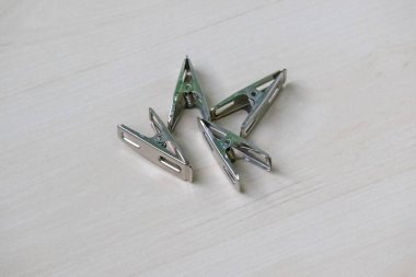 Ahşap yüzeyde duran dört parlak paslanmaz çelik mandal. Çamaşır, el işi ya da organizasyon için ideal. Mandal ya da elbise askısı olarak da bilinir..