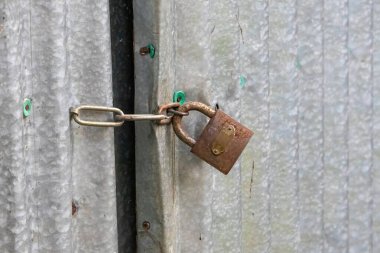 Bangladeş 'teki bir köyün galvanize demir çarşaf kapısının eski paslı kilidi. Zincirleme bağlantı ve kapı kilidini kapat.