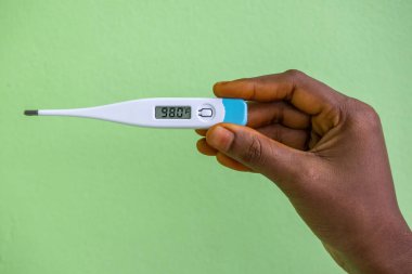 Yeşil arka planda dijital termometre tutan bir kadın el. Vücut sıcaklığı 98.0 F. Sağlık ve Sıhhat kavramı.