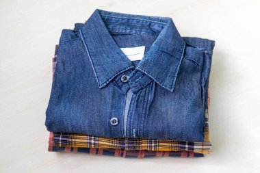 Bir sürü katlanmış erkek pamuk gömleğinin yakın çekimi. Parlak ahşap bir arka planda, rengarenk bir moda elbisesi yığını. Dokuları ve günlük stili renklendiriyor..