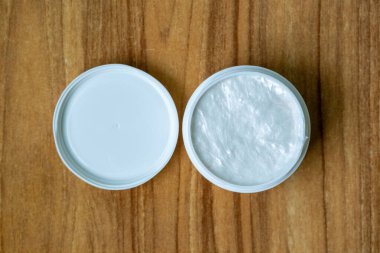 Açık bir kadının yüz kremi kabının en üst görüntüsü. Kapağı yanında, sıcak bir ahşap zemin üzerine kurulmuş. Güzellik ürünü reklamı için harika..