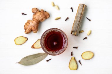 Bir cam fincanda geleneksel sağlıklı siyah ya da kırmızı çay, saçılmış kokulu yapraklar, kakule, tarçın, karanfil ve zencefil gibi aromatik baharatlar içerir. Üst görünüm.