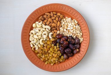 Badem, kaju fıstığı, fıstık, hurma ve kuru üzümlerden oluşan sağlıklı beslenme çeşidi doğal kilden bir tabakta güzelce sunuluyor. Sağlıklı olmak ve besleyici atıştırmalıklar için ideal. Üst görünüm.