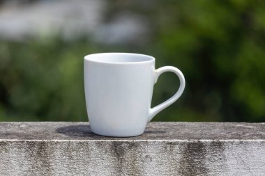 Boş beyaz seramik bir kupa yıpranmış bir duvarda bulanık, doğal bir arka planı olan.