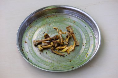 Yemek yedikten sonra paslanmaz çelik bir tabakta bir yığın tavuk kemiği ve kırıntılar. Lezzetli bir kızarmış tavuk yemeğinin kalıntıları, arta kalan bir konsepti gösteriyor..