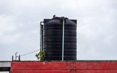 Bangladeş 'te bir binanın çatısındaki siyah plastik su tankının arkasında bulutlu bir gökyüzü var..