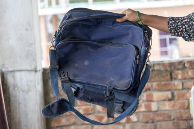 Hasarlı, yırtık, çok amaçlı bir çantayı tutan bir kadının yakın çekimi. Bu çok yönlü çanta bir zamanlar okul, seyahat, ofis işi ve dizüstü bilgisayar çantası ya da sırt çantası olarak kullanılırdı..