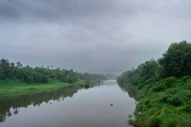 Hindistan 'da yeşil ağaçları ve dağları olan sakin bir nehrin manzarası.