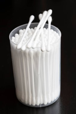 Beyaz pamuklu kulak temizleme tomurcukları siyah arka planda güzelce konteynırda yerleştirilmiş.