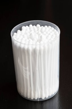 Beyaz pamuklu kulak temizleme tomurcukları siyah arka planda güzelce konteynırda yerleştirilmiş.