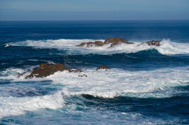 Kıyı kayalarına vuran beyaz köpüklü kaynayan uzun okyanus dalgaları (deniz manzarası))