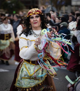Çingene gibi giyinmiş yaşlı bir kadın karnavalda kurdeleli tef çalıyor.