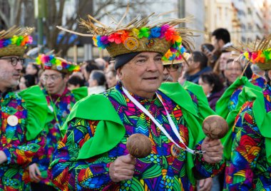 Bir karnavalda elinde marakas tutan parlak elbiseli yaşlı bir adam..