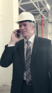 Fabrikada yürüyen ve telefonla konuşan kasklı bir iş adamı. Dikey video