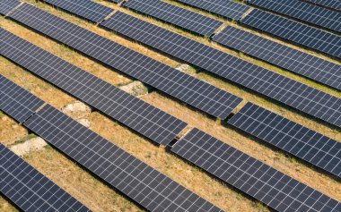 Kuru çimen alanındaki sıra sıra dizilmiş güneş panellerinin hava görüntüsü
