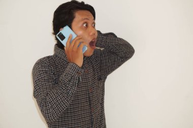 Genç Asyalı adam telefonla ararken şok olmuş yüz ifadesi sergiliyor