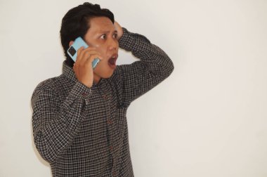 Genç Asyalı adam telefonla ararken şok olmuş yüz ifadesi sergiliyor