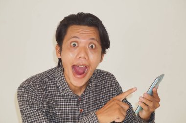 Siyah tişörtlü genç Asyalı adam beyaz arka planda izole akıllı telefondan şaşırıyor..