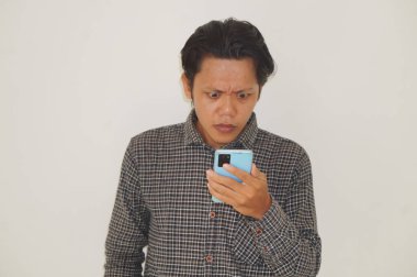 Siyah tişörtlü genç Asyalı adam beyaz arka planda izole akıllı telefondan şaşırıyor..