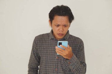 Siyah tişörtlü genç Asyalı adam beyaz arka planda izole akıllı telefondan şaşırıyor..