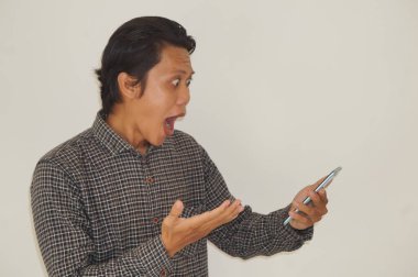 Siyah tişörtlü genç Asyalı adam beyaz arka planda izole akıllı telefondan şok oluyor..