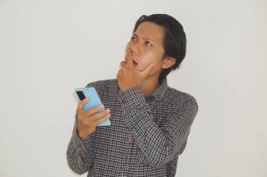 Genç Asyalı adam cep telefonu tutarken bir şeyler düşünüyor. izole edilmiş beyaz arkaplan