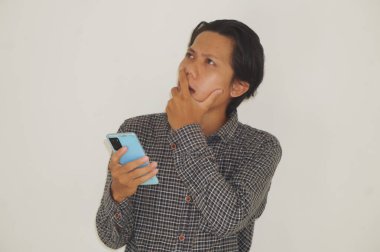 Genç Asyalı adam cep telefonu tutarken bir şeyler düşünüyor. izole edilmiş beyaz arkaplan