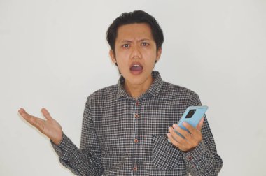 Genç Asyalı adam cep telefonu tutarken kafası karışık bir yüz ifadesi sergiliyor