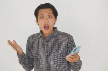 Genç Asyalı adam cep telefonu tutarken kafası karışık bir yüz ifadesi sergiliyor