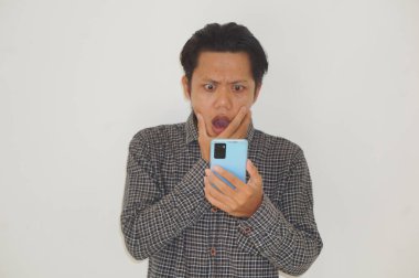 Siyah tişörtlü genç Asyalı adam beyaz arka planda izole edilmiş akıllı telefona bakarken şaşırdı.