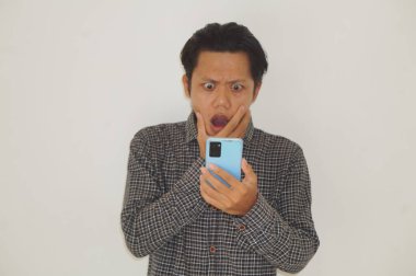 Siyah tişörtlü genç Asyalı adam beyaz arka planda izole edilmiş akıllı telefona bakarken şaşırdı.