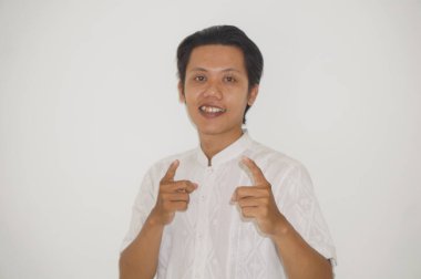 Beyaz tişörtlü genç Asyalı adam kamerayı göstererek mutlu ve gülümsüyor.