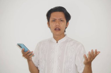 Genç Asyalı adam cep telefonu tutarken kafası karışık bir yüz ifadesi sergiliyor