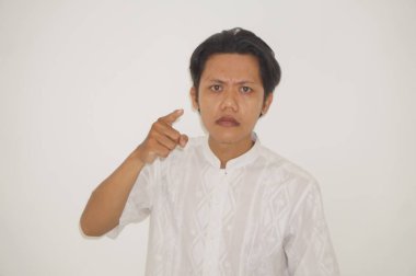 Genç Asyalı adam kamerayı göstererek kızgın beyaz gömlek giyiyor.