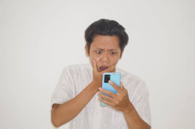 Beyaz gömlekli genç Asyalı adam beyaz arka planda izole edilmiş akıllı telefona bakarken şaşırdı.