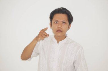 Genç Asyalı adam kamerayı göstererek kızgın beyaz gömlek giyiyor.