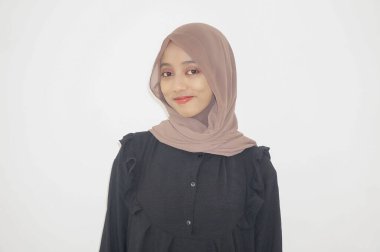 Siyah elbiseli ve tesettürlü güzel Asyalı kadın beyaz arka planda kendinden emin bir şekilde kameraya bakıyor.