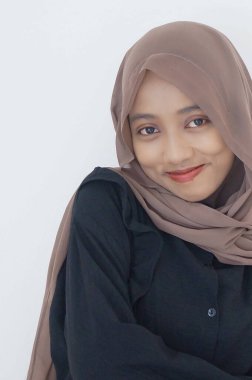 Siyah elbiseli ve tesettürlü güzel Asyalı kadın beyaz arka planda kendinden emin bir şekilde kameraya bakıyor.