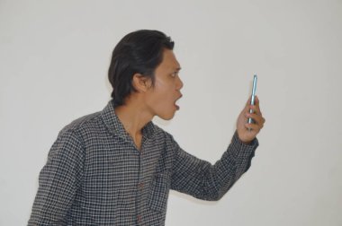 Siyah tişörtlü genç Asyalı adam beyaz arka planda izole edilmiş akıllı telefona bakarken şaşırdı.