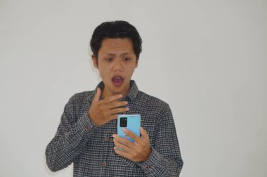 Siyah tişörtlü genç Asyalı adam beyaz arka planda izole edilmiş akıllı telefona bakarken şaşırdı.