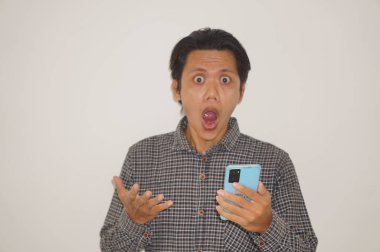 Siyah tişörtlü genç Asyalı adam beyaz arka planda izole edilmiş akıllı telefona bakarken şaşırdı..