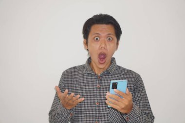 Siyah tişörtlü genç Asyalı adam beyaz arka planda izole edilmiş akıllı telefona bakarken şaşırdı..