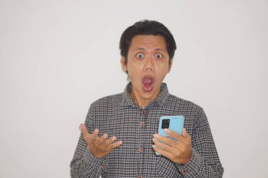 Siyah tişörtlü genç Asyalı adam beyaz arka planda izole edilmiş akıllı telefona bakarken şaşırdı..