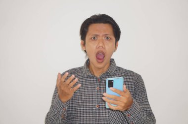 Siyah tişörtlü genç Asyalı adam beyaz arka planda izole edilmiş akıllı telefona bakarken şaşırdı..