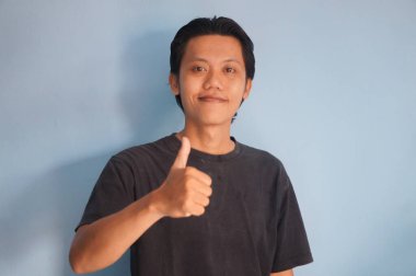 Asyalı adam kameraya gülümsüyor. Siyah tişört giyiyor. Baş parmağını gösteriyor.